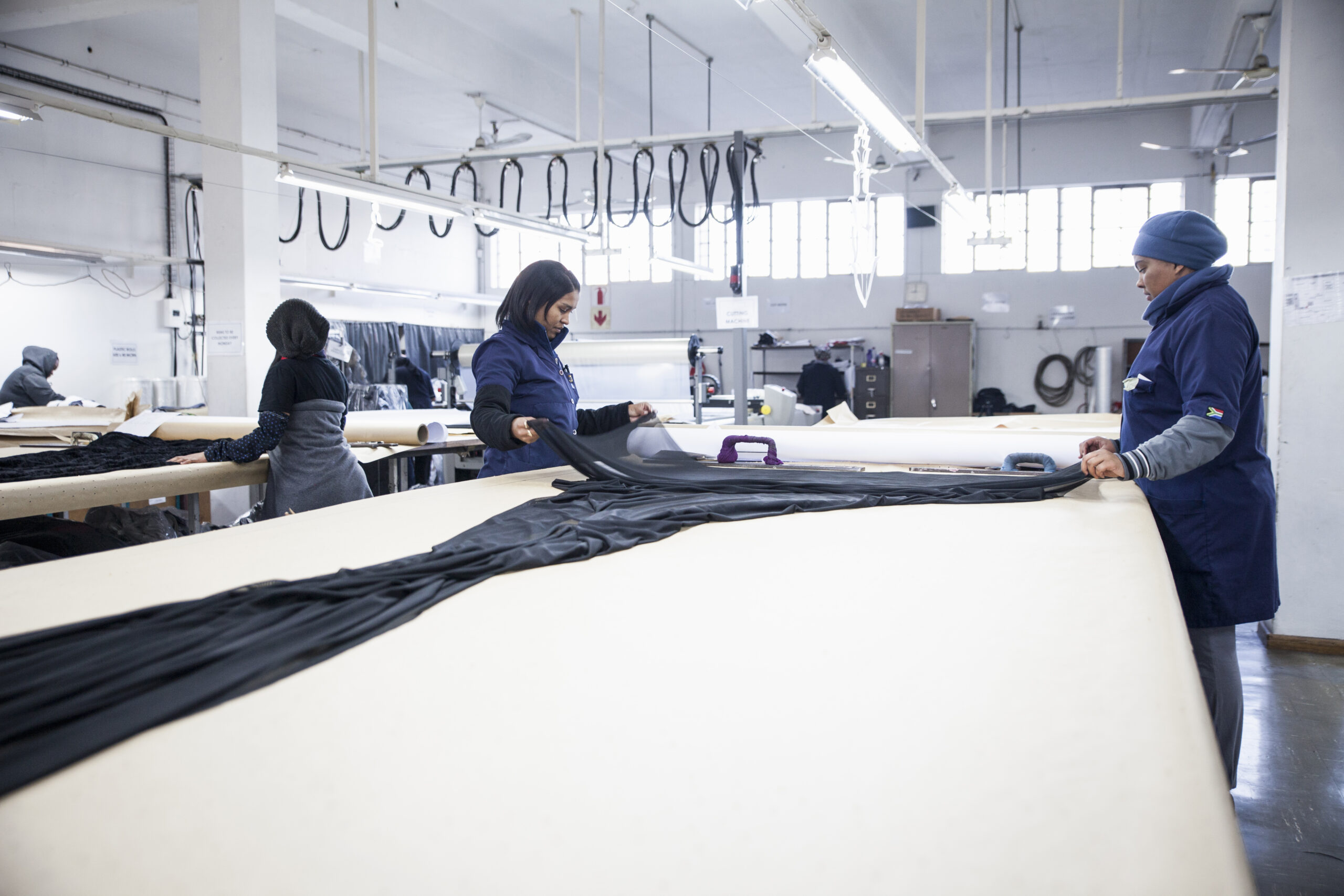 Factory workers unrolling textiles on work table in clothing factory