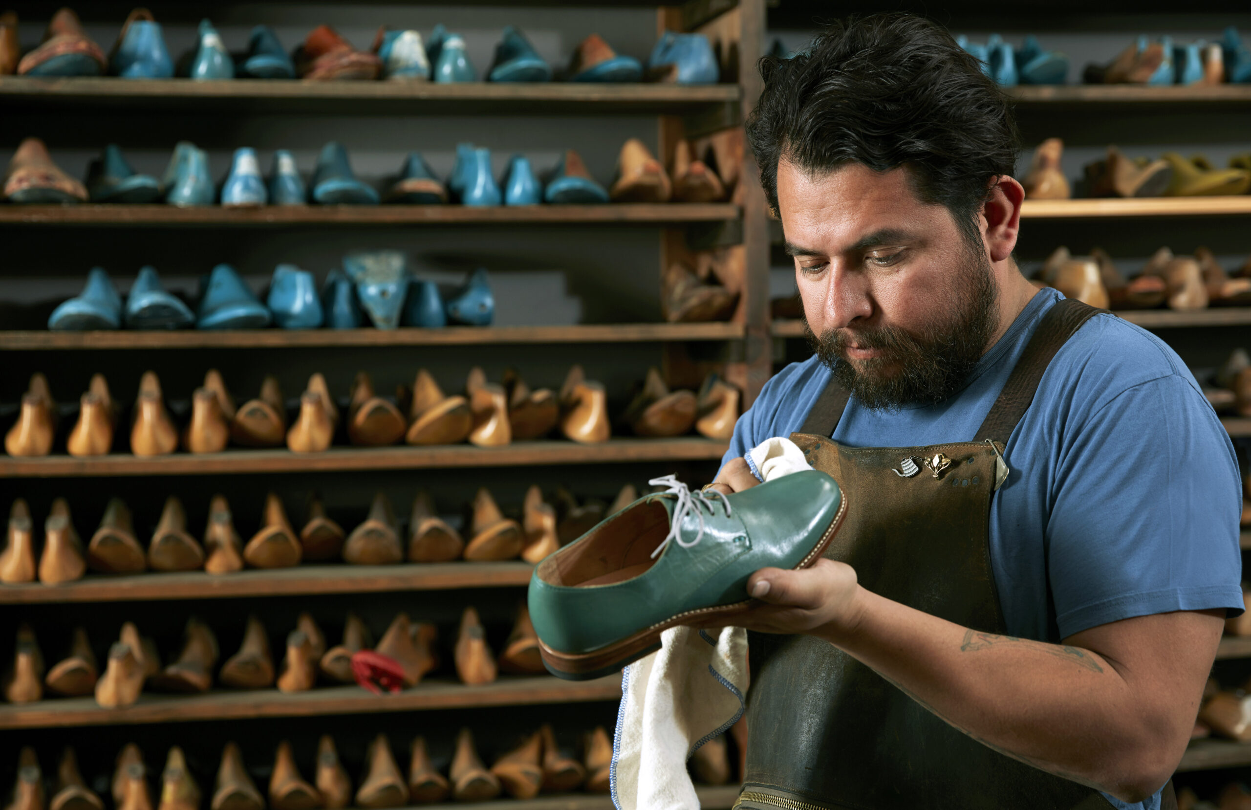 Male cobbler in traditional shoe shop polishing green brogue