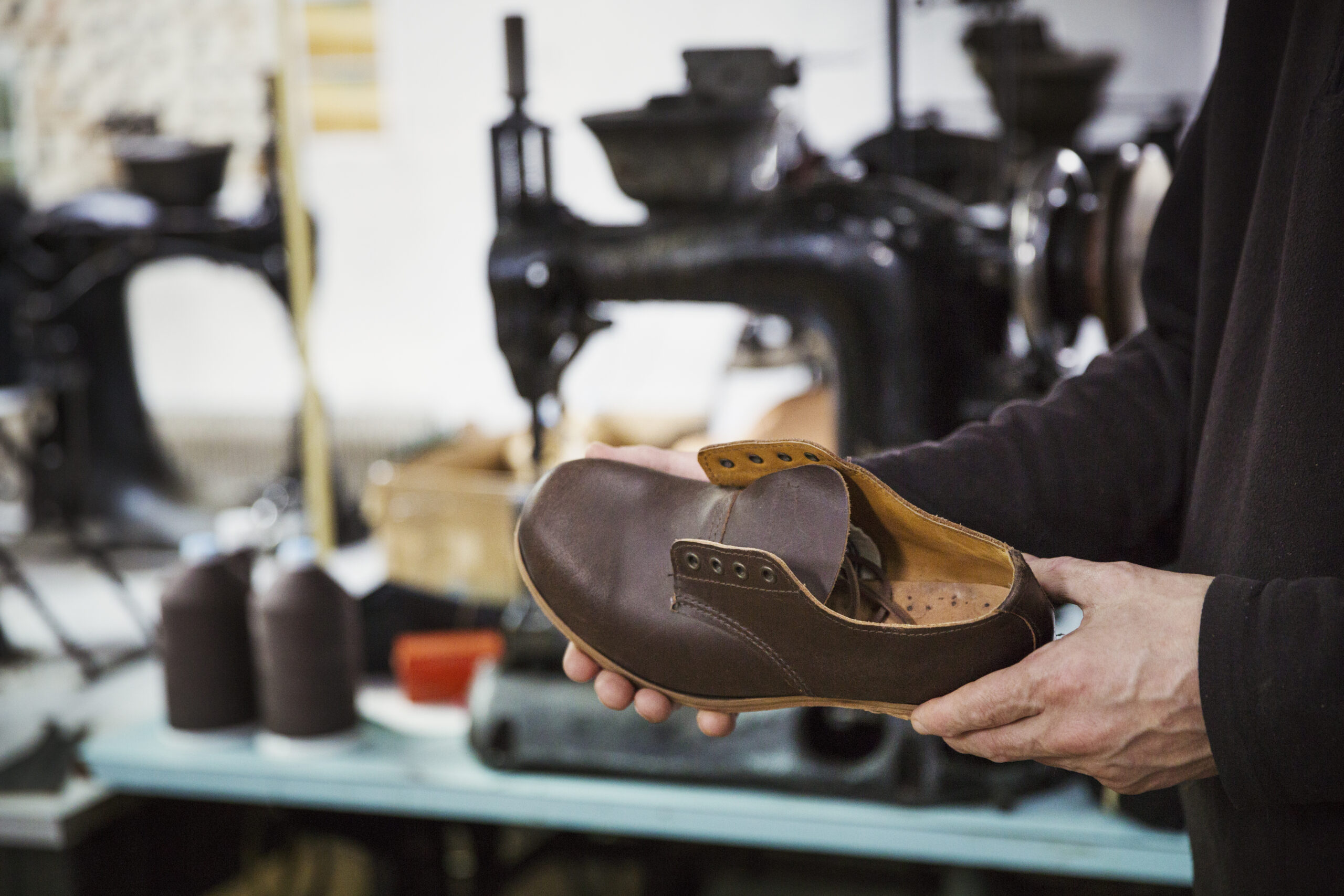 Man standing in a shoemaker’s workshop, holding brown leather shoe.,Footwear manufacture,England
