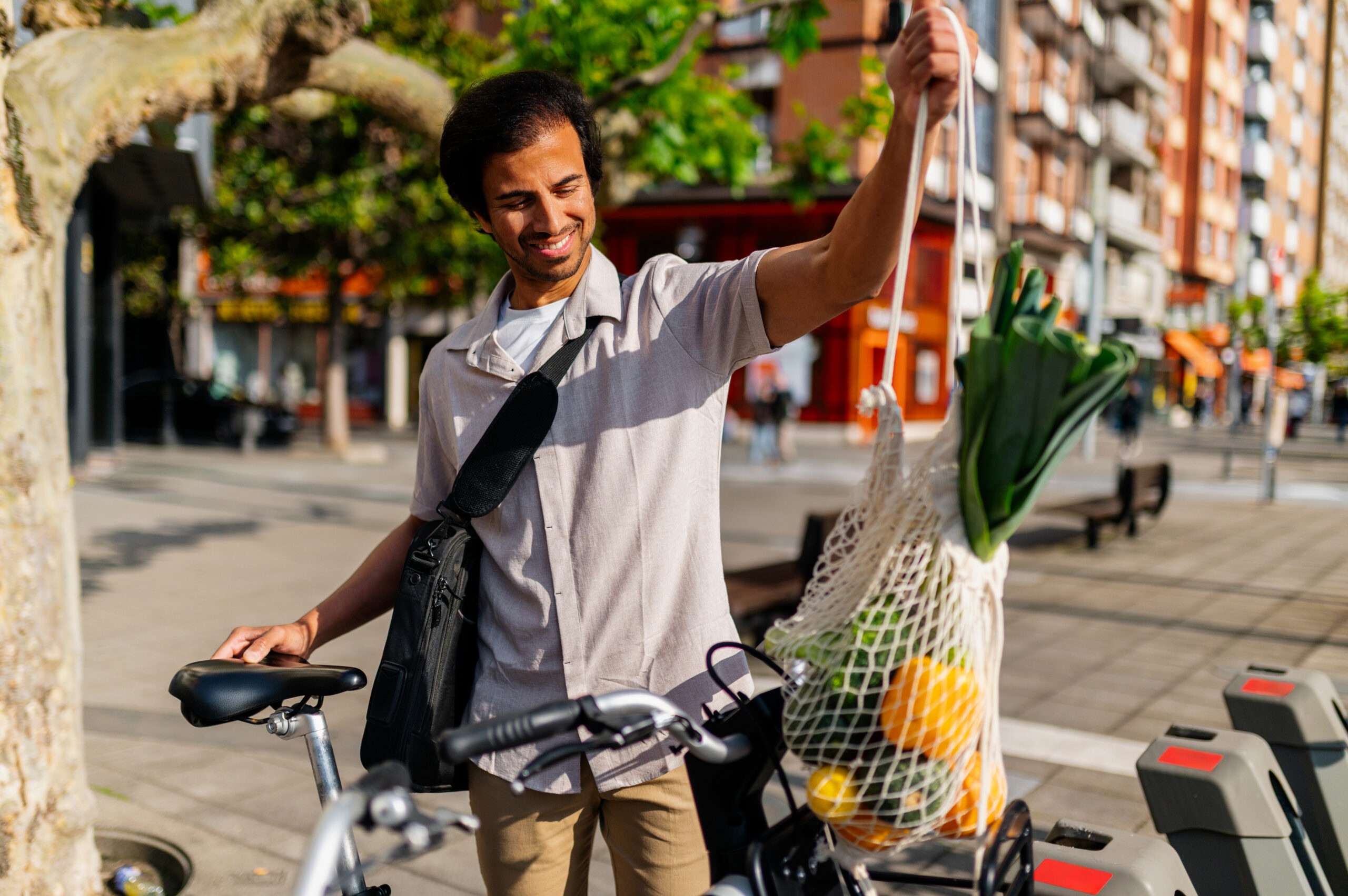 Young businessman holding reusable shopping bag with groceries next to his bicycle
