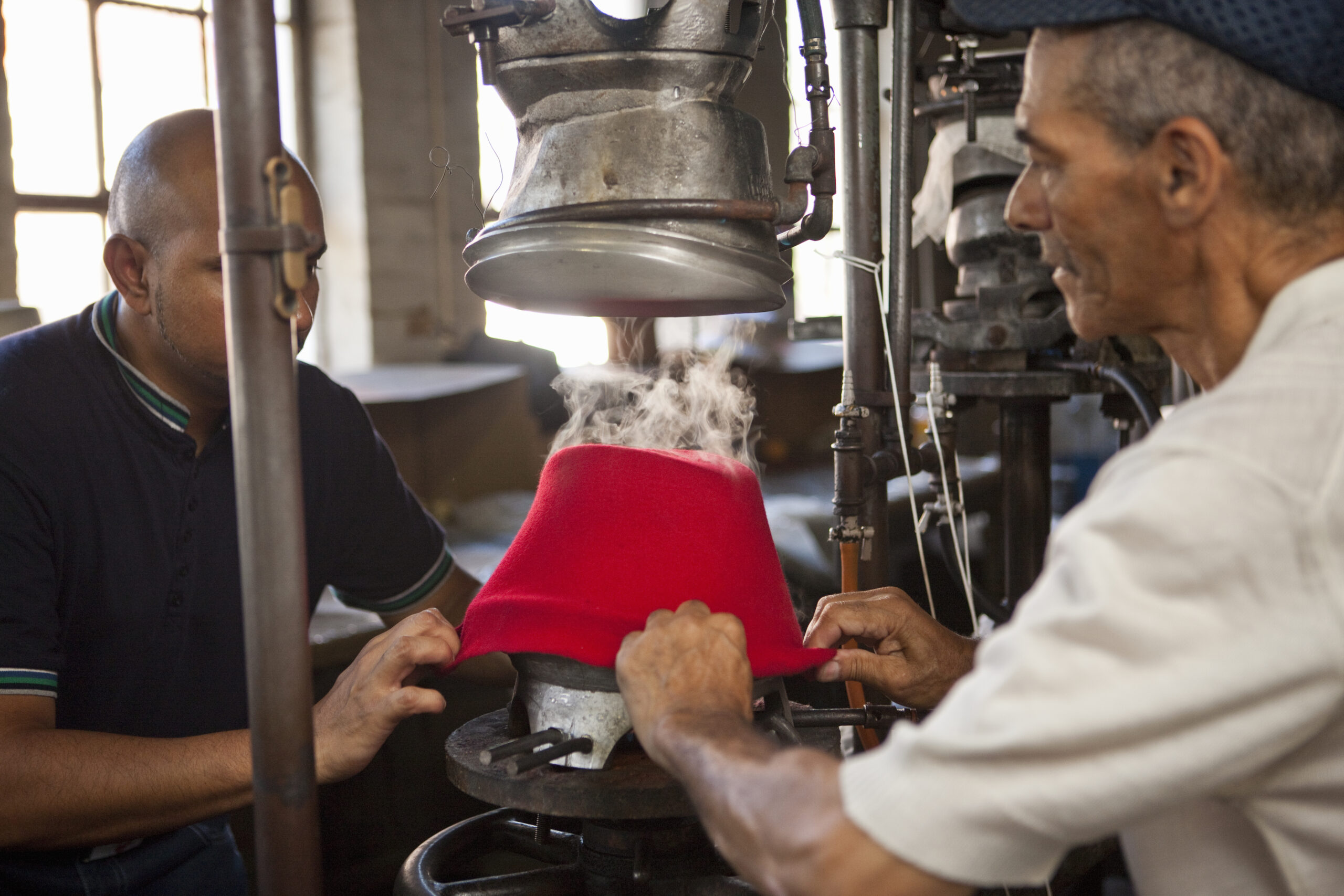 Hat makers pulling fabric onto mould in workshop