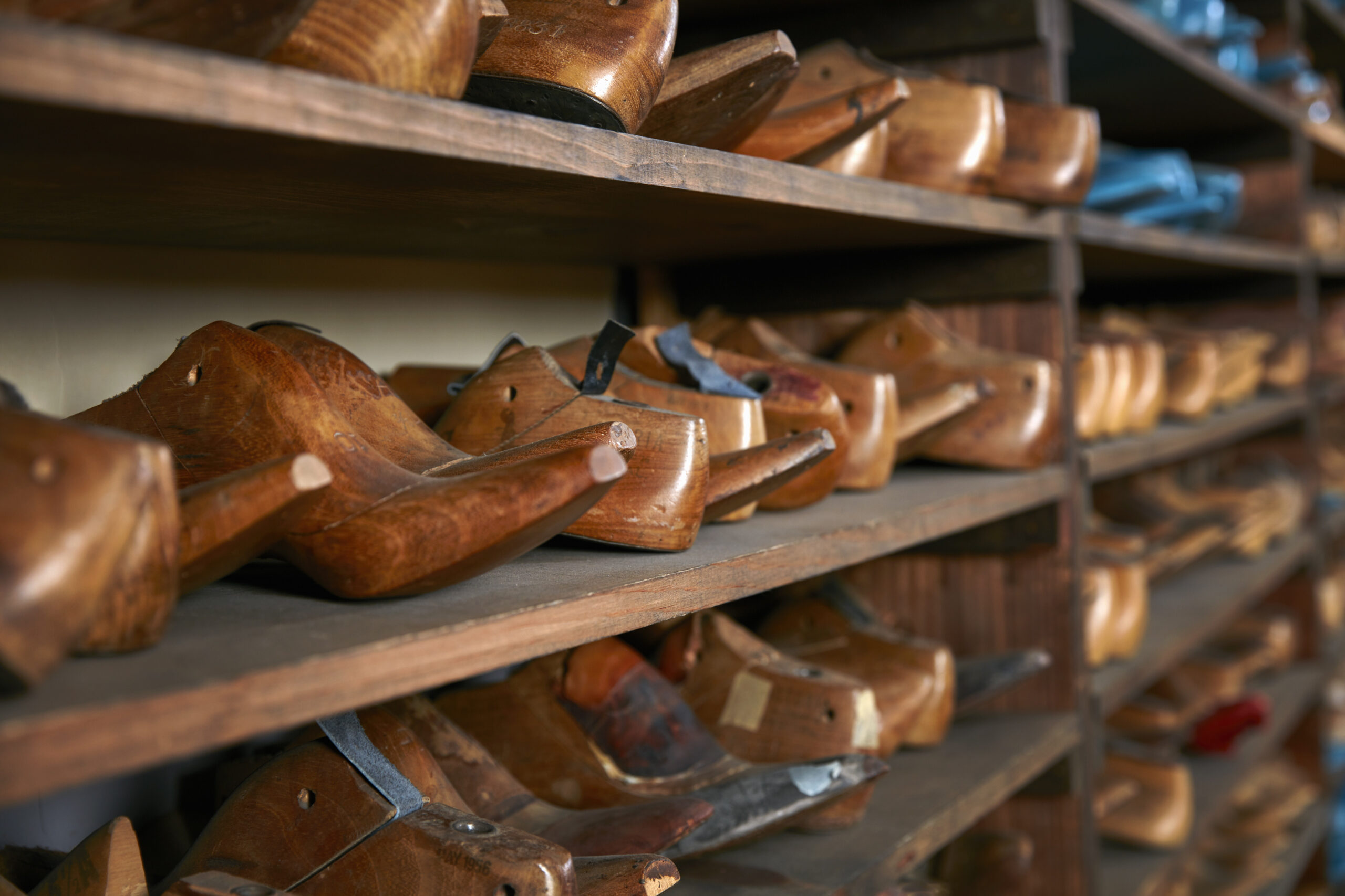 Rows of old wooden shoe lasts on shelves in traditional shoe shop, selective focus