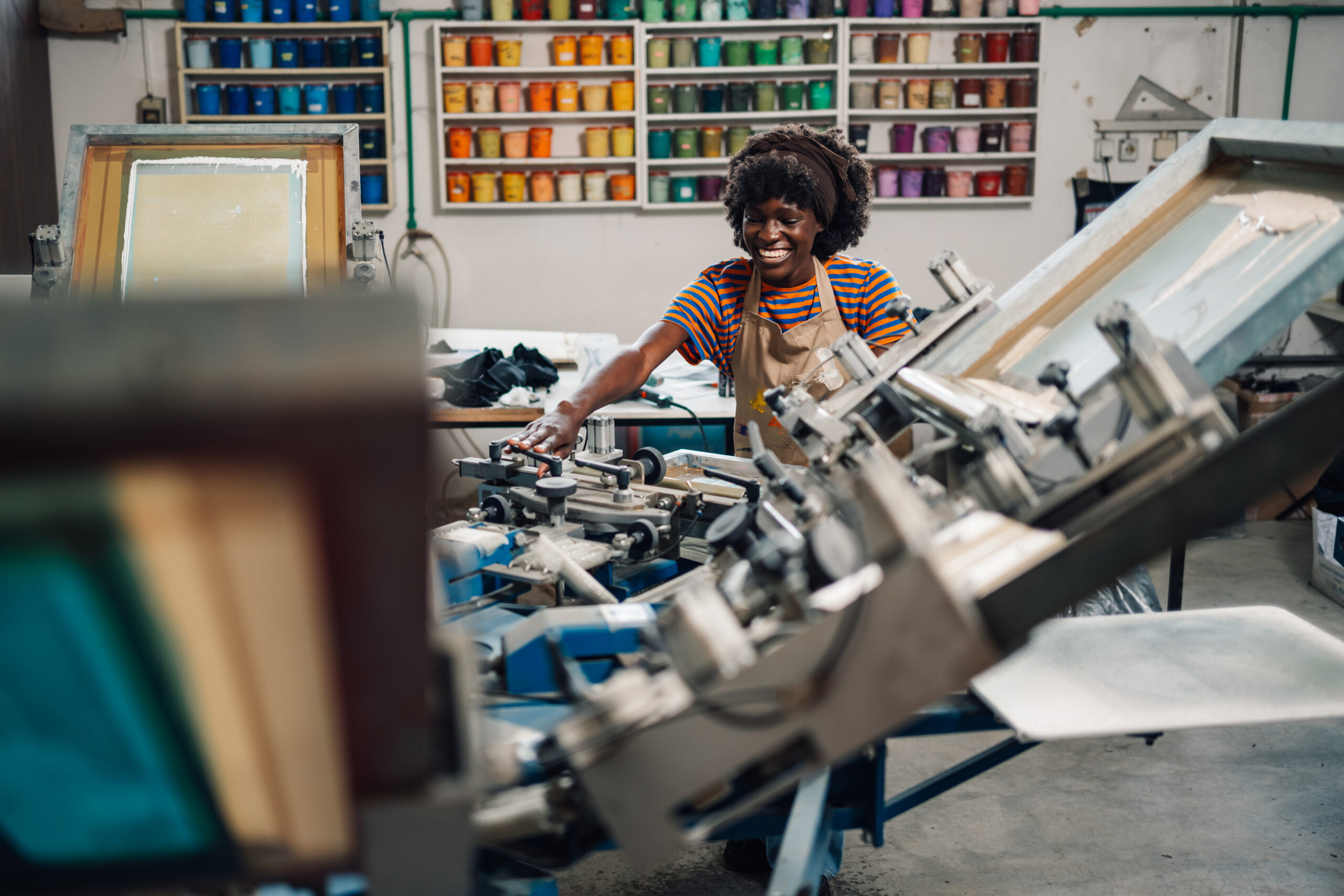 Diverse graphic worker adjusting printing machine at printing workshop